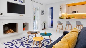 Un salon moderne avec une cheminée, un téléviseur fixé au mur et un coin cuisine équipé de tabourets de bar.