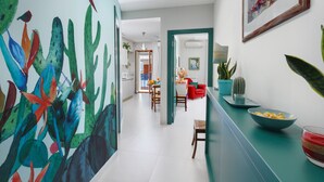 A hallway with a colorful mural, a dining area with a red chair, and a kitchen with a cactus plant. - Estate4home - Esé (Sorrento)