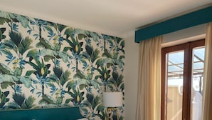 A hotel room with a large bed, a view of the outdoors, and a tropical-themed wallpaper. - Resort Ravenna (Massa Lubrense)