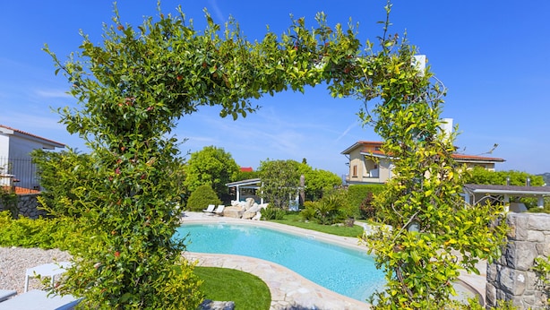 A swimming pool surrounded by stone walls and lush greenery, with a clear blue sky above. - Resort Ravenna (Massa Lubrense)