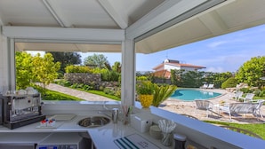 A kitchen with a coffee machine, sink, and a view of a backyard with a pool and outdoor furniture. - Resort Ravenna (Massa Lubrense)
