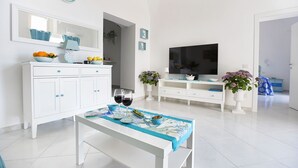 Un salon moderne avec un canapé blanc, une table basse, un téléviseur et un coin repas avec une table dressée pour deux personnes.