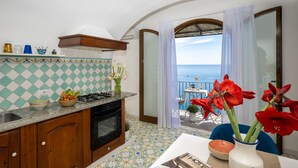 A kitchen with a view of the sea, a dining area with a table and chairs, and a balcony with a table and chairs. - Estate4home - Emeri Positano (Positano)