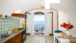 A kitchen with a view of the sea, a dining area with a table and chairs, and a small balcony with a table and chairs. - Estate4home - Emeri Positano (Positano)