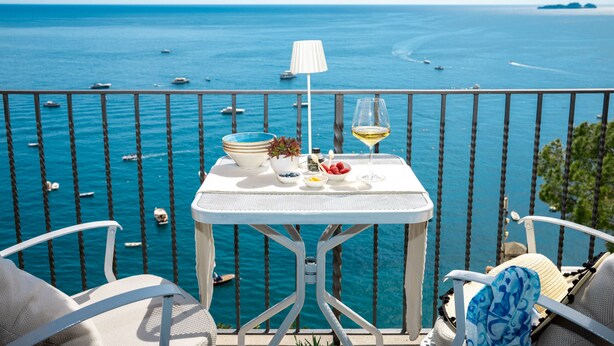 A balcony with a table set for two, overlooking a clear blue sea with boats. - Estate4home - Emeri Positano (Positano)