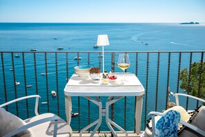 En balkon med et bord dækket til to, med udsigt over et klart, blåt hav med både.