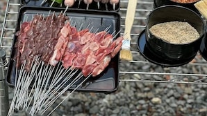 Churrasqueira montada com espetos de carne e legumes, um pincel e recipientes com temperos.