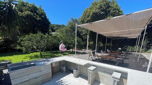 Um pátio externo com área de estar em concreto, uma pérgula para dar sombra e um comedouro suspenso para pássaros.