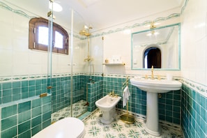 A bathroom with a toilet, bidet, and sink, featuring green and white tiles and a mirror.