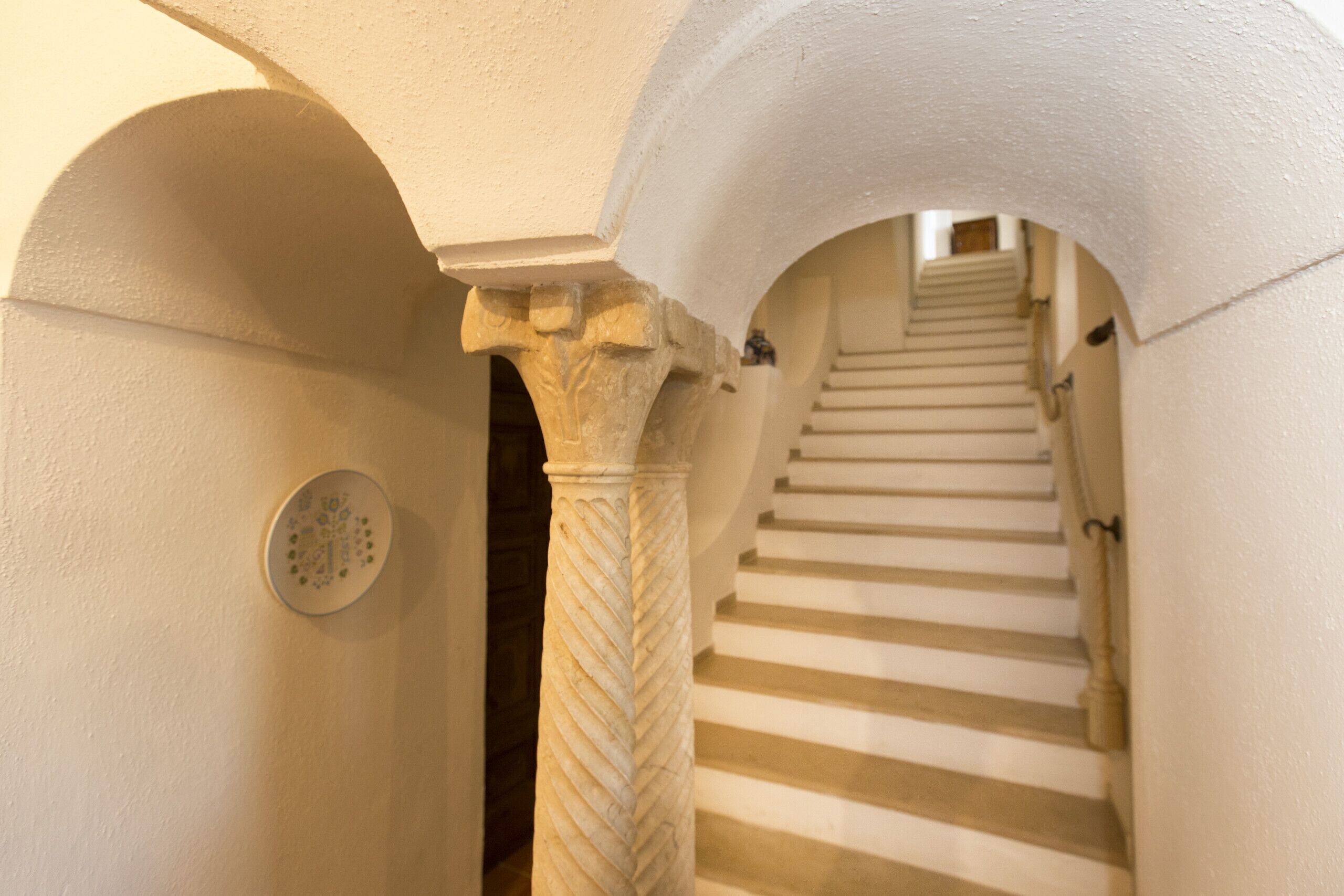 Eine Treppe mit weißen Stufen und einer Säule aus Stein mit einer geschnitzten Musterung.