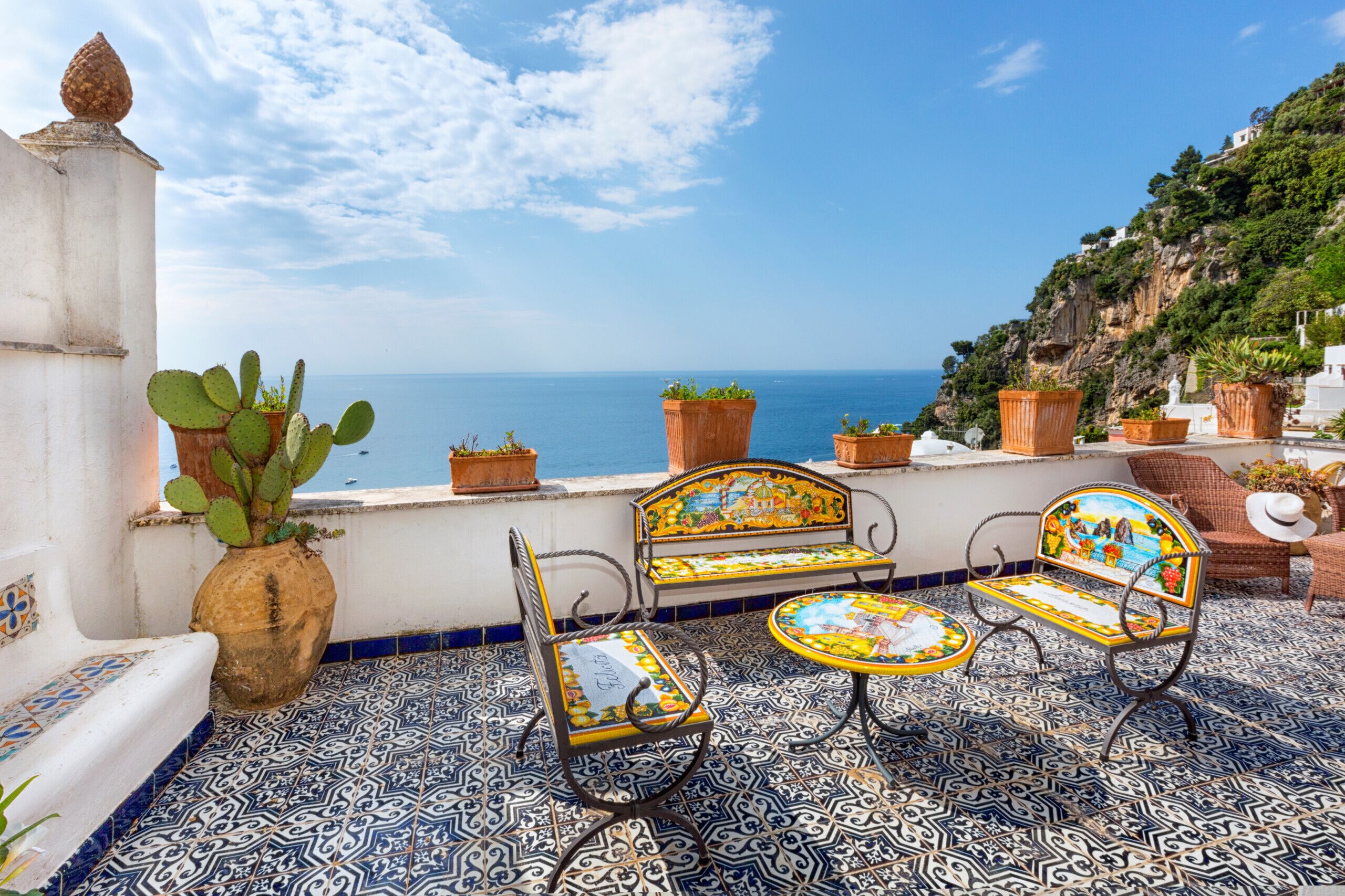 A terrace with patterned flooring, a bench, a table, and potted plants.