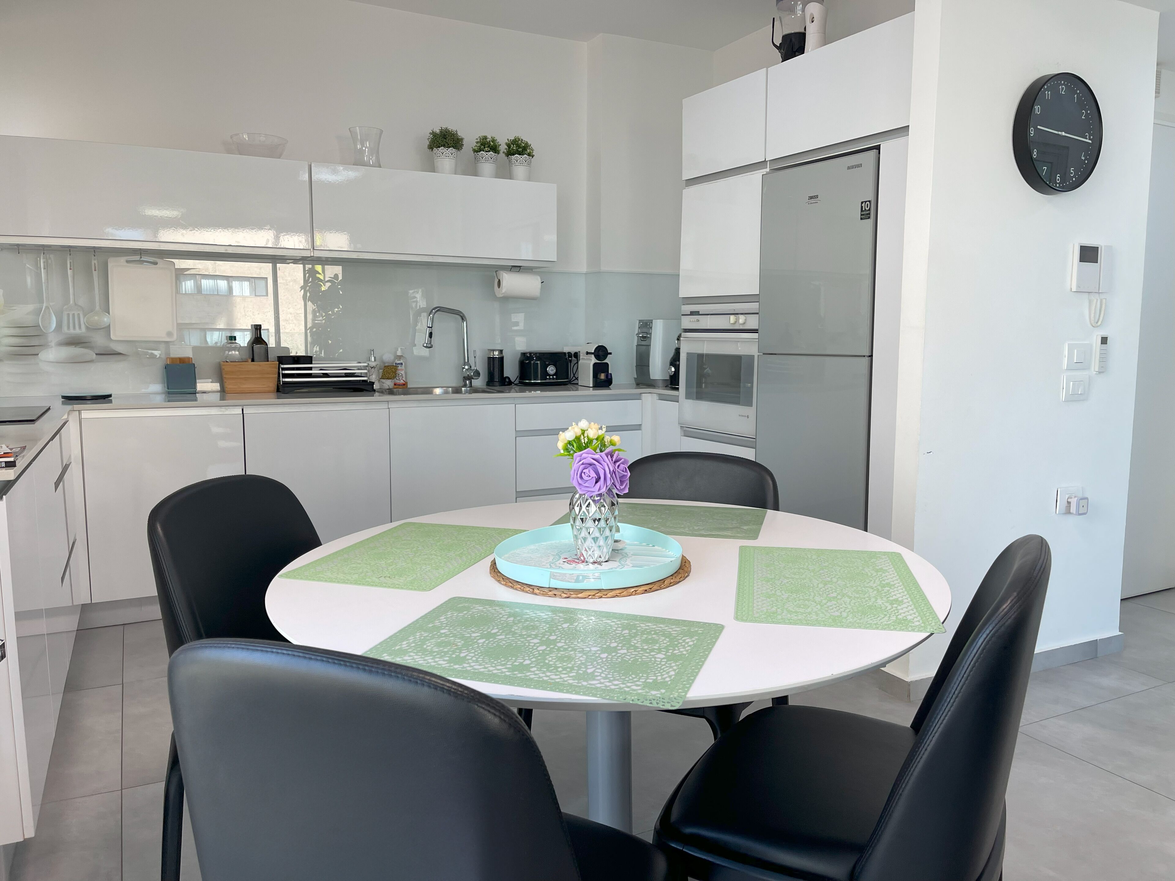 A modern kitchen with white cabinets, a stainless steel refrigerator, and a clock on the wall.