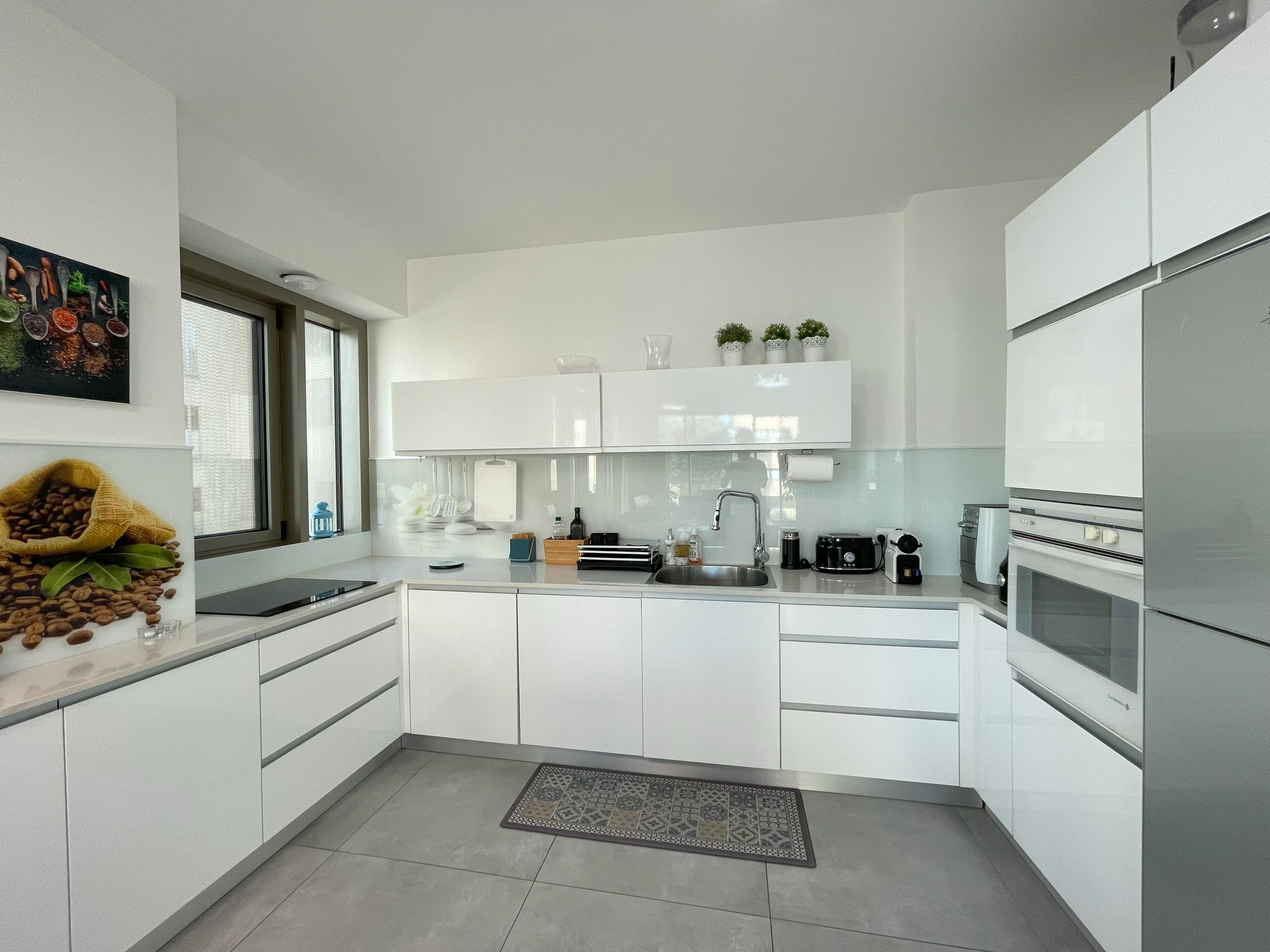 Una cucina moderna con mobili bianchi, un frigorifero in acciaio inossidabile e una grande isola con un lavello.