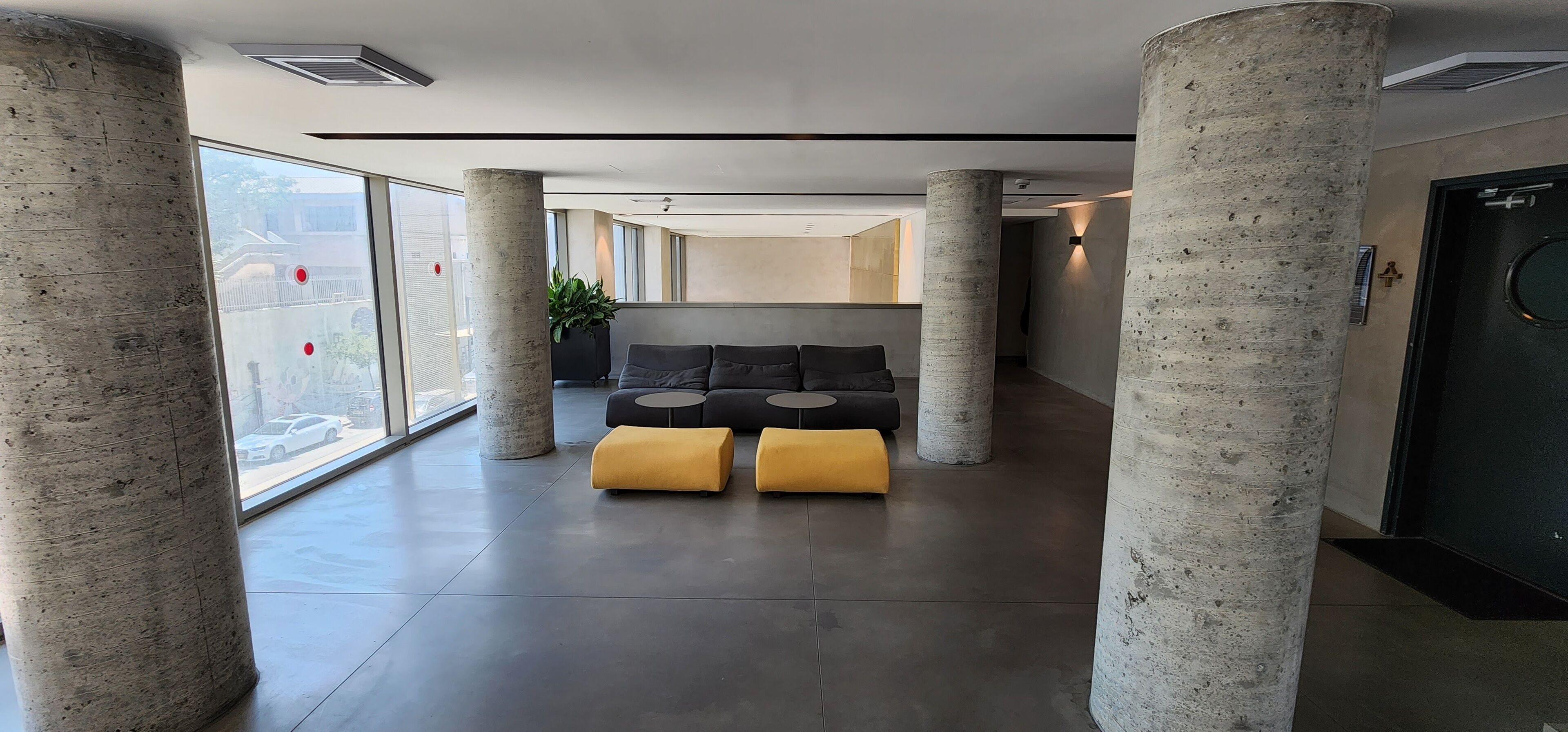 Un hall d’entrée moderne avec des piliers en béton, un canapé avec des coussins et une plante en pot.