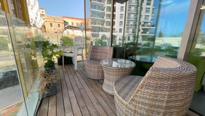 A balcony with wicker furniture and a glass table, overlooking a cityscape with modern buildings. - AirTLV - Luxury Apartment Port of Jaffa (Tel Aviv)