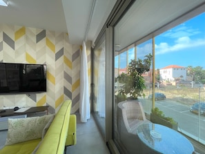 A modern living room with a sofa, a TV, and a balcony with a view of the city.