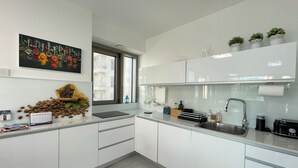 A modern kitchen with white cabinets, a stainless steel sink, and a window with a view of buildings. - AirTLV - Luxury Apartment Port of Jaffa (Tel Aviv)