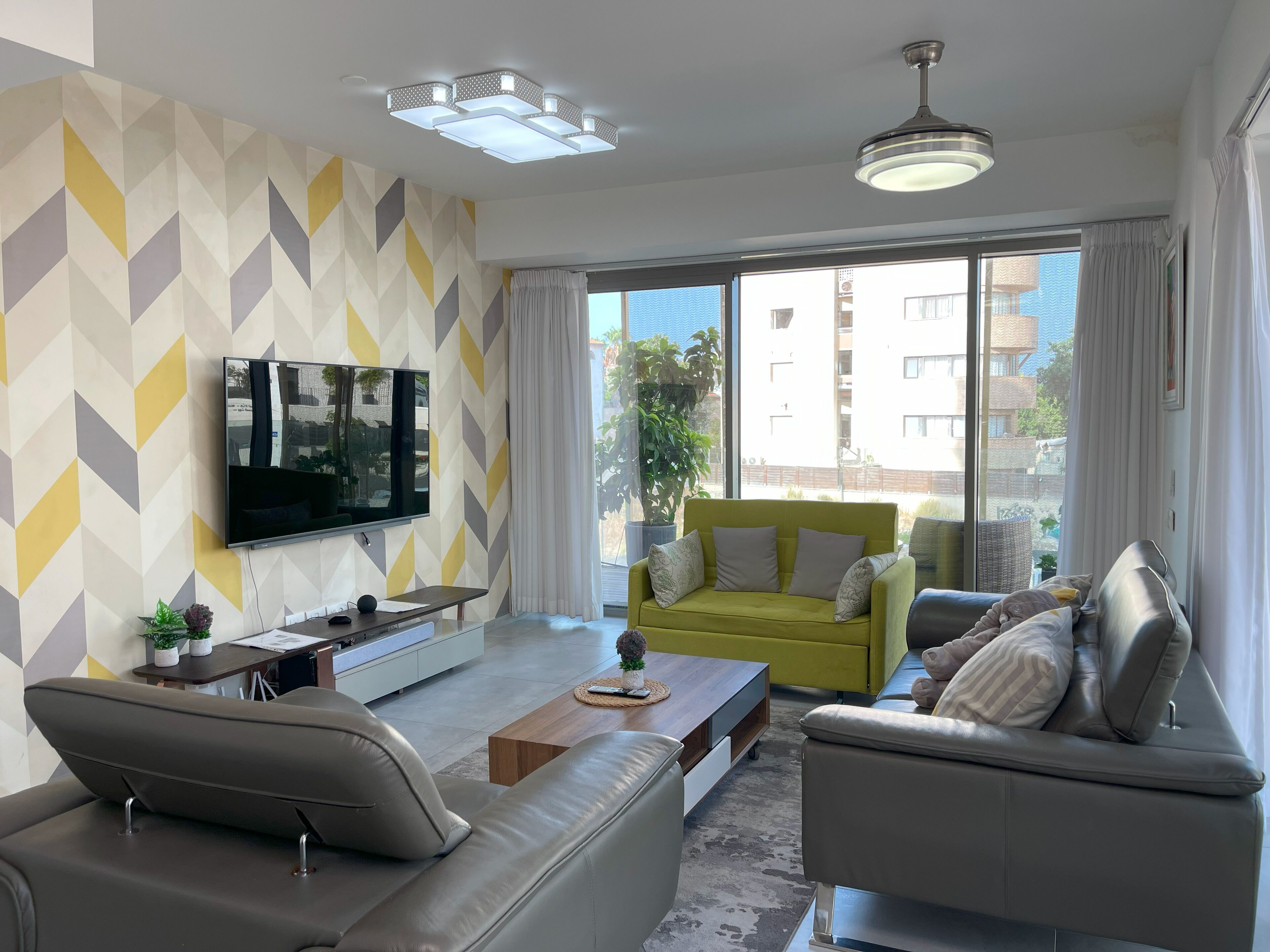 A modern living room with a flat-screen TV, a sofa, a coffee table, and a yellow armchair.