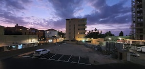 A parking lot with a white car, surrounded by buildings with multiple floors and balconies, under a twilight sky.