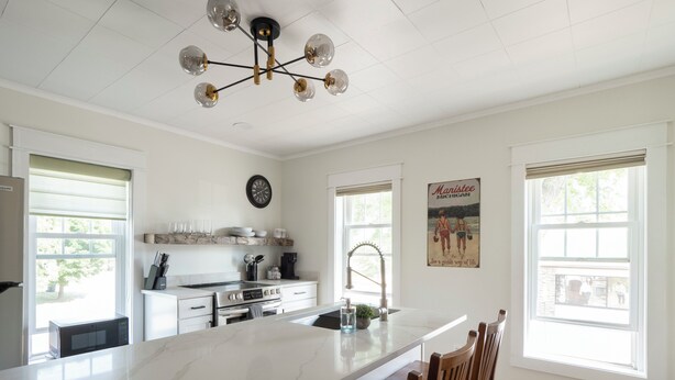 A kitchen with a large island, white cabinetry, a stainless steel range, and a unique chandelier. - Cozy 1+ Bedroom Haven with Charm and is a block from downtown! (Manistee)
