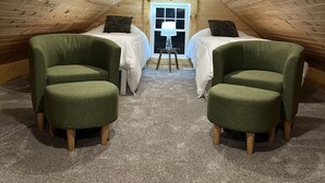 A cozy attic bedroom with two beds, a small table, and two green armchairs. - Cozy 1+ Bedroom Haven with Charm and is a block from downtown! (Manistee)