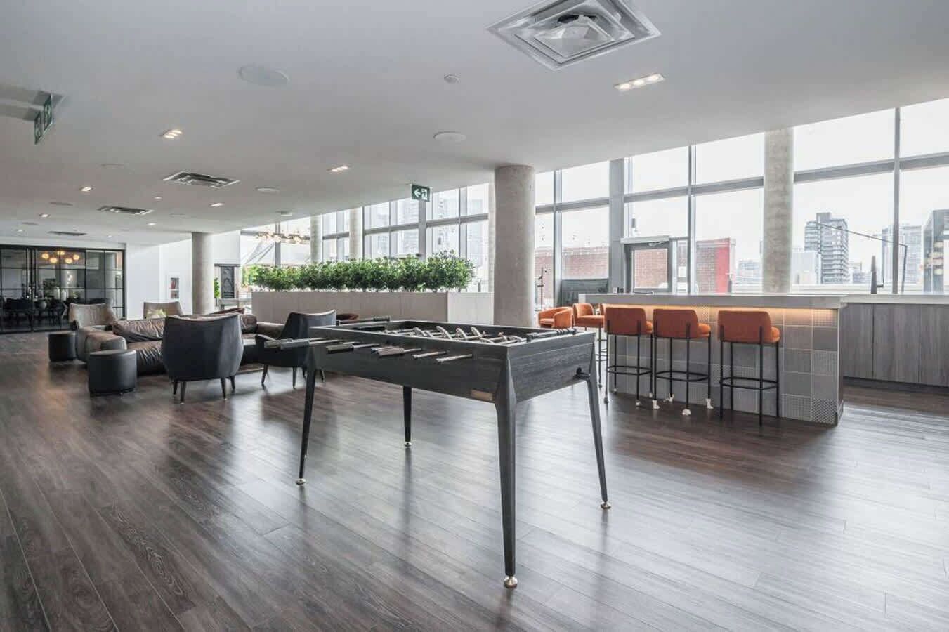 A spacious lobby with a foosball table, comfortable seating, a bar area, and large windows offering city views.