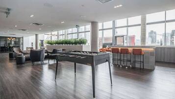 A spacious lobby with a foosball table, comfortable seating, a bar area, and large windows offering city views.