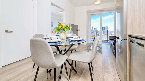 A modern dining area with a glass table, grey upholstered chairs, and a vase of flowers. - Union Towers Condo with City Views and Patio (Kitchener)