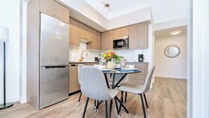 A modern kitchen with wooden cabinets, stainless steel appliances, and a dining area with a table set for four. - Union Towers Condo with City Views and Patio (Kitchener)