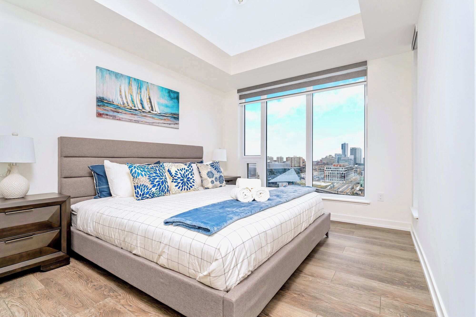 Quarto moderno com uma cama grande, vista para a cidade e um quadro na parede.
