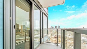 Un balcón con puertas y ventanas de vidrio amplias, que ofrece vistas de un paisaje urbano con edificios y obras de construcción.