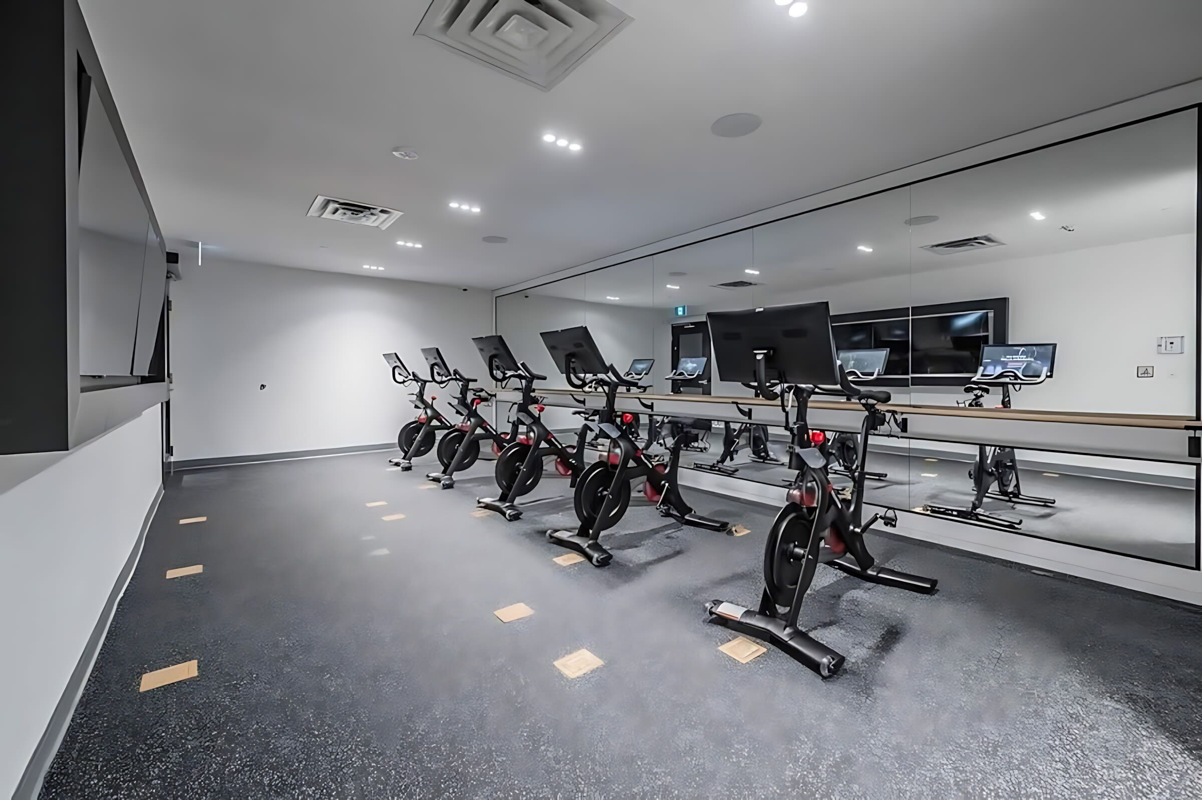 Une salle de sport équipée de plusieurs vélos d’exercice et d’appareils de cardio, d’un grand miroir et d’un long banc.