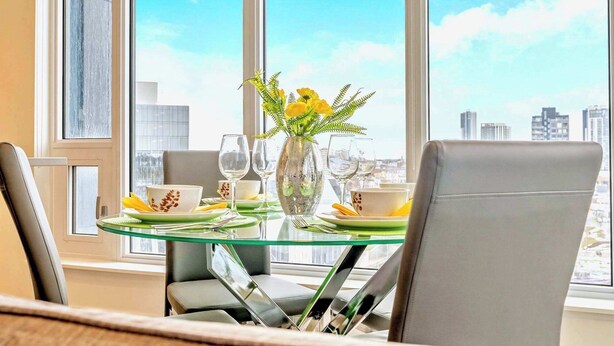 Un comedor con una mesa de vidrio, sillas y un florero con flores amarillas.