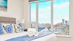 Un dormitorio moderno con un amplio ventanal, una cama bien tendida y vistas a la ciudad.