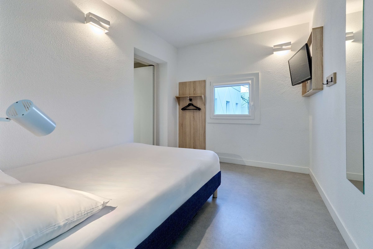 A modern bedroom with a bed, a hanging light, a TV mounted on the wall, and a window.