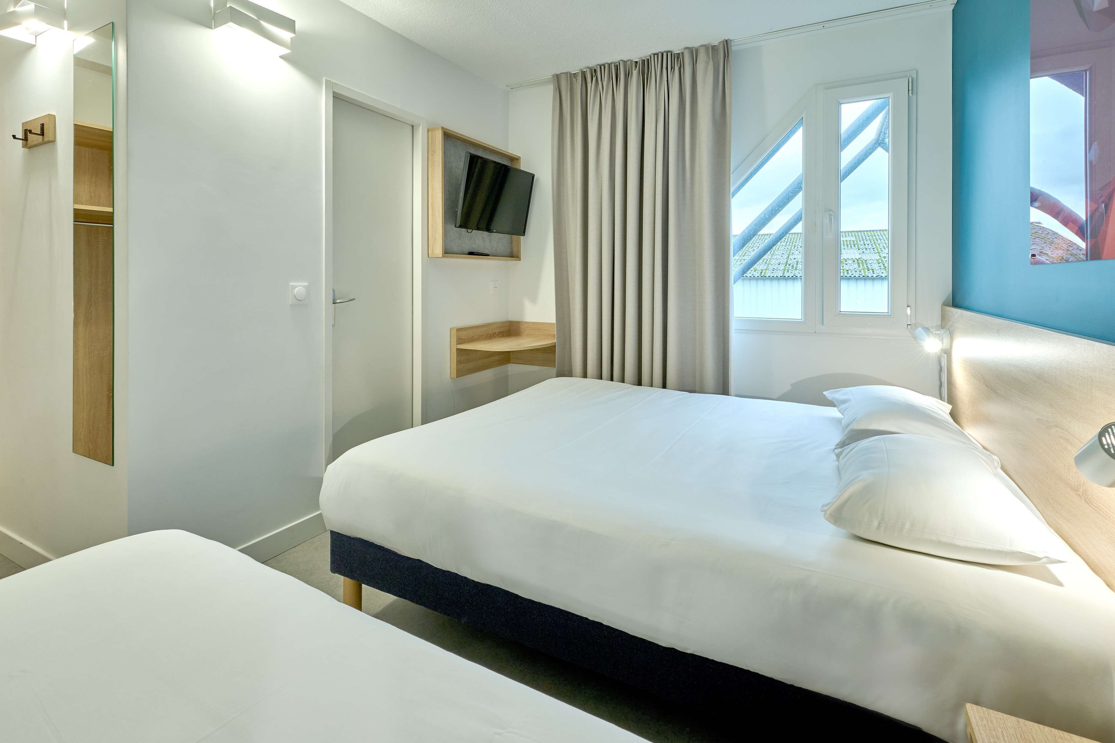 Habitación de hotel con cama, televisor montado en la pared, ventana con cortinas y vistas al exterior.
