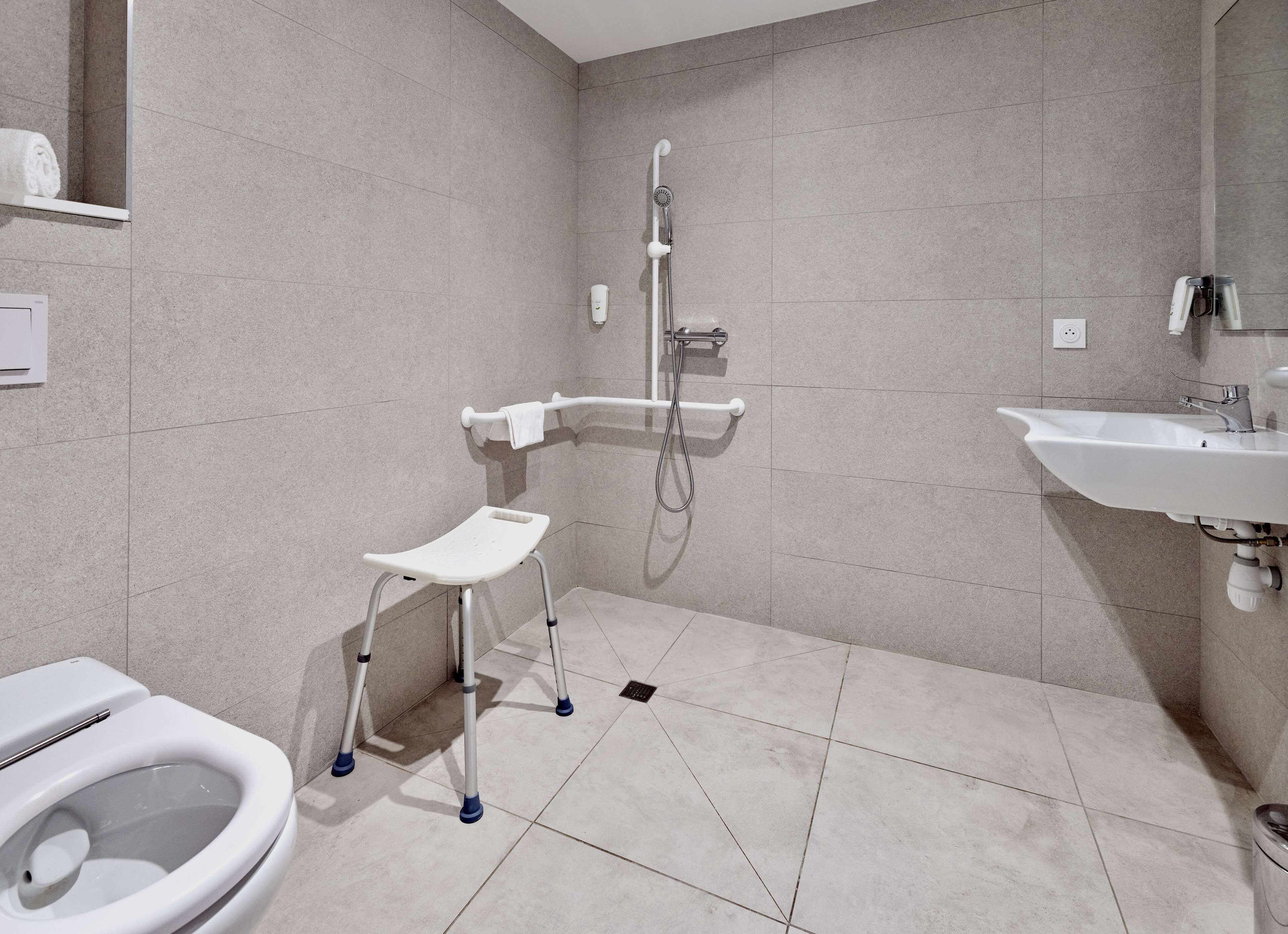 A modern bathroom with a toilet, a shower with a handheld showerhead, a sink, and a small step stool.