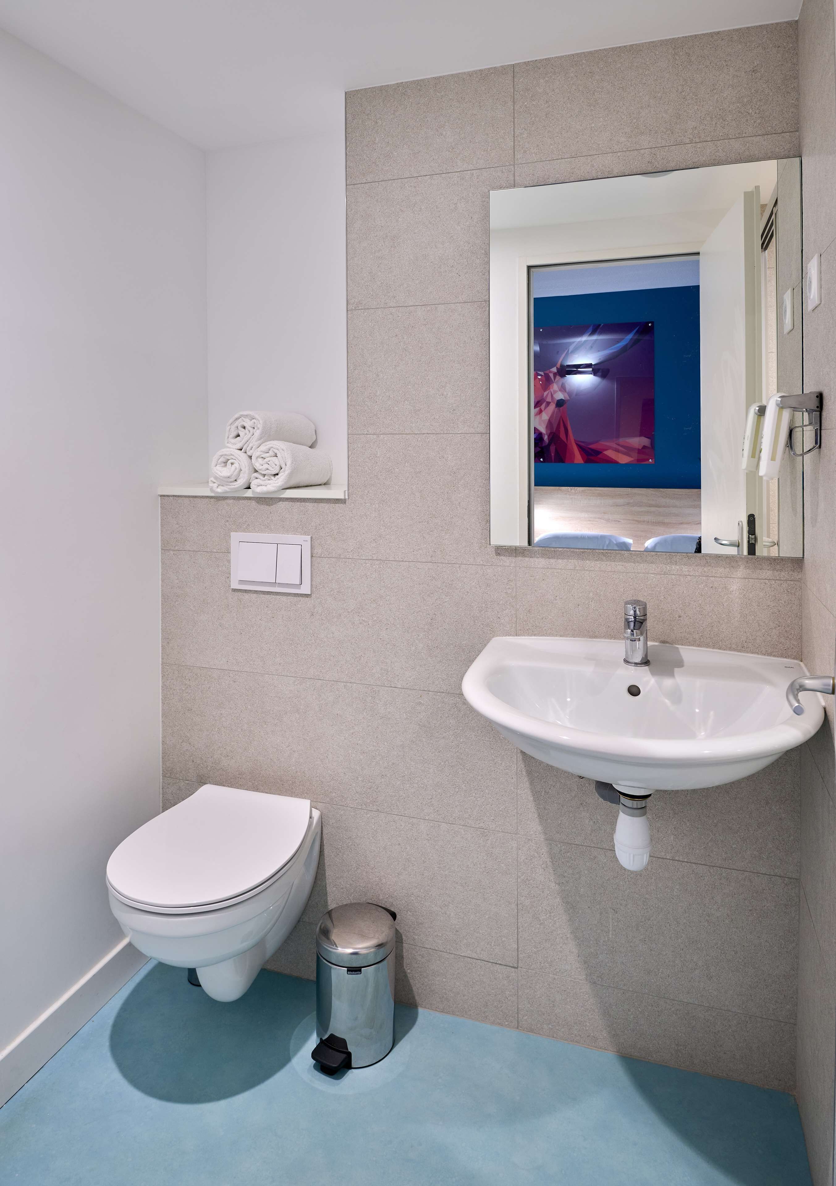 Un baño moderno con inodoro blanco, lavabo y cubo de basura.