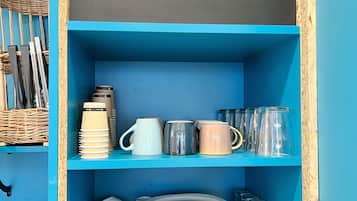 A blue shelf unit with a chalkboard sign reading "à TABLE!" and various kitchenware including plates, cups, and mugs.