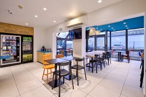 A modern cafe with a variety of seating options, including tables and chairs, and a vending machine. - Kyriad ECO - Narbonne Sud (Narbonne)