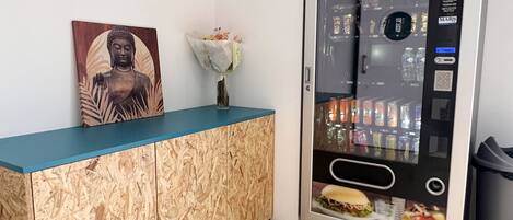 A reception area with a wooden cabinet, a Buddha statue, a vase with flowers, and a vending machine.