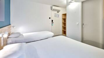 Quarto de hotel com duas camas de solteiro, um guarda-roupa, aparelho de ar condicionado e porta com puxador.