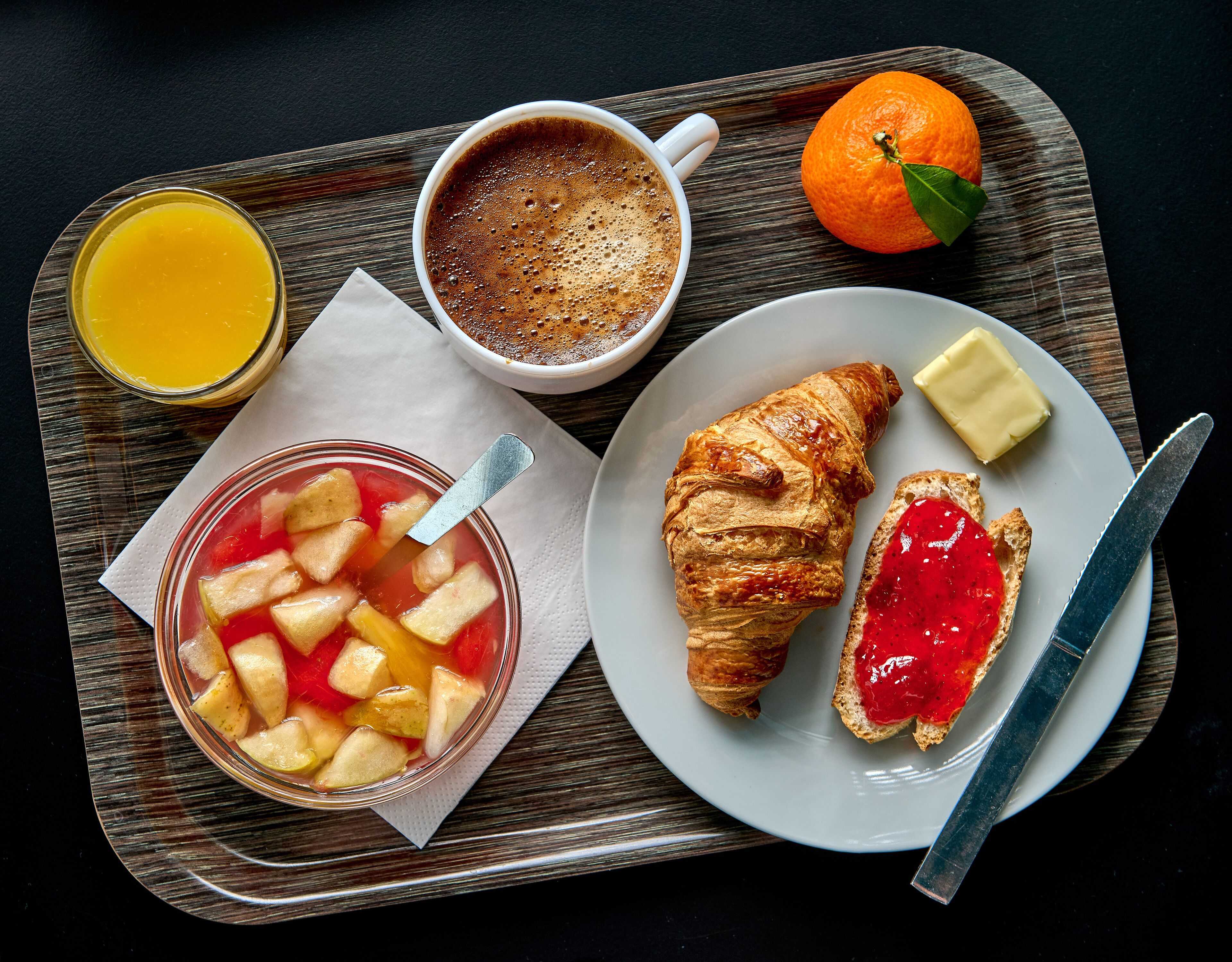 Een dienblad met een croissant, jam, boter, een glas sinaasappelsap en een kop koffie.