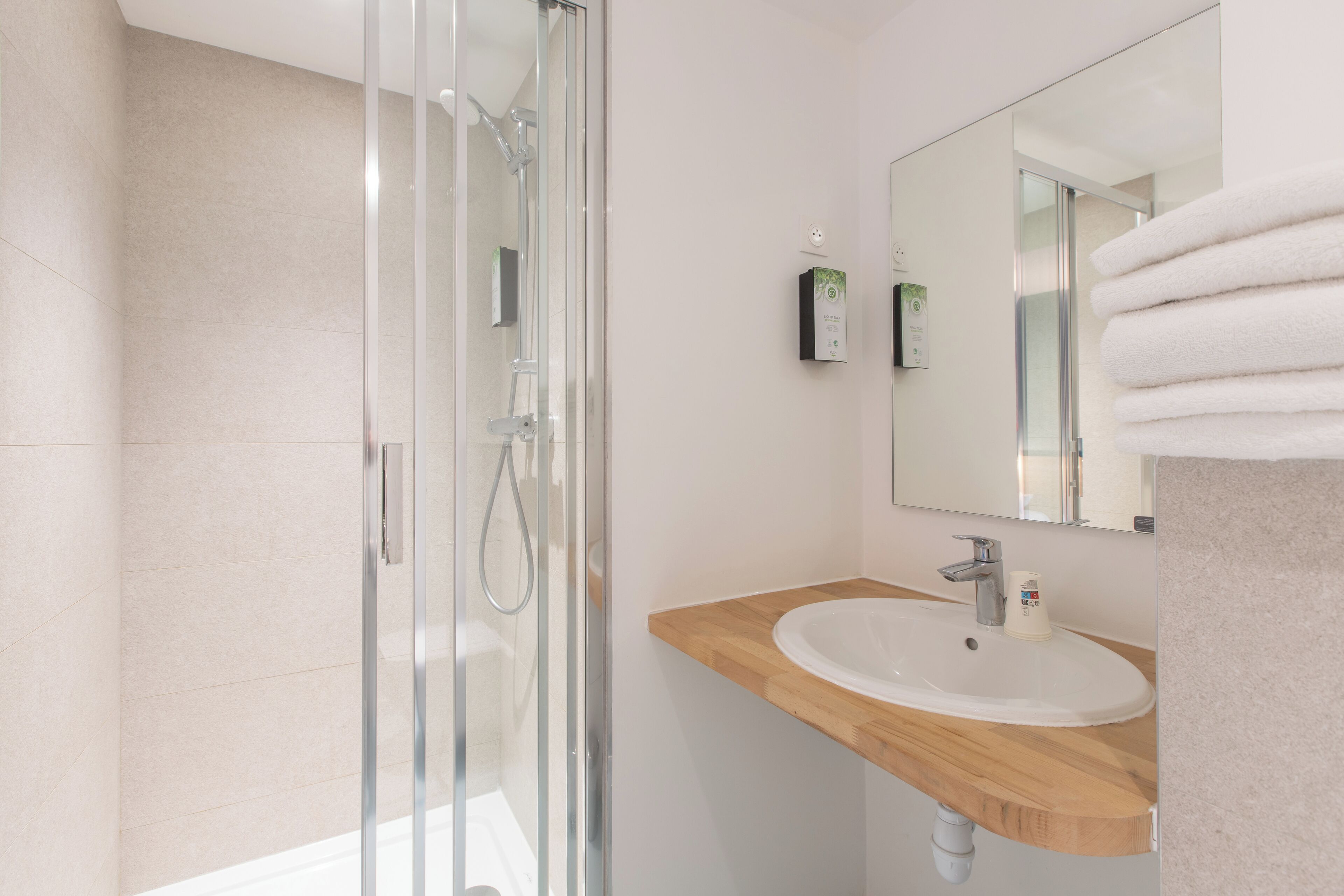 Un baño moderno con ducha envuelta en vidrio, tocador de madera y un espejo grande.