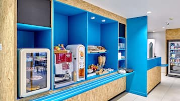 Una estación de café moderna con diseño azul y de madera, que incluye una máquina de café, un dispensador de jugo y un refrigerador.