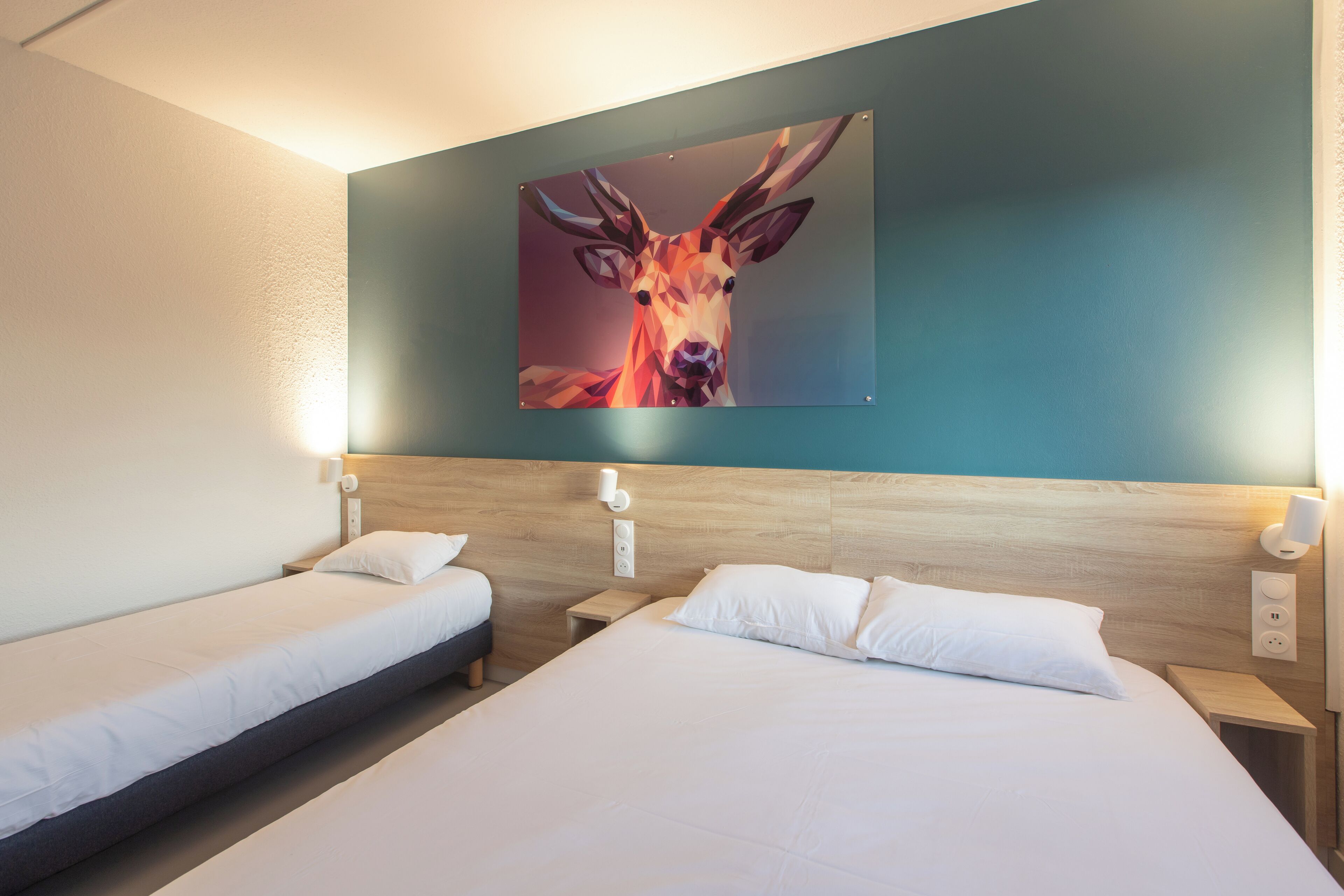 A hotel room with two single beds, a wooden headboard, a wall-mounted painting of a deer, and bedside lamps.