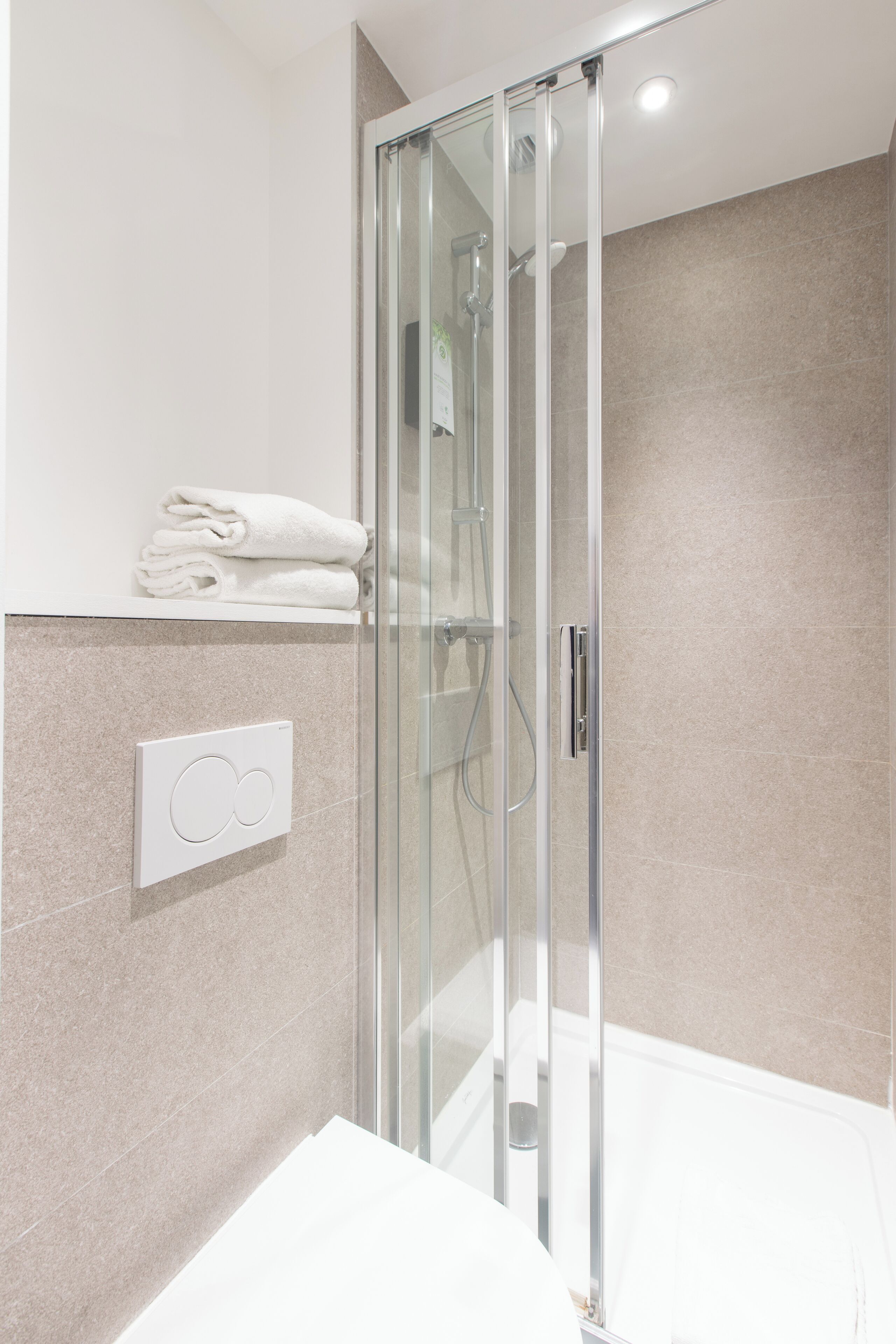 Un baño moderno con ducha envuelta en vidrio, un lavamanos blanco y un perchero para toallas.