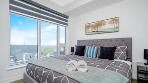 Een moderne slaapkamer met een groot bed, uitzicht op de stad en een schilderij aan de muur.