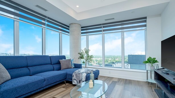 Een moderne woonkamer met een blauwe bank, een glazen salontafel en grote ramen met uitzicht over de stad.