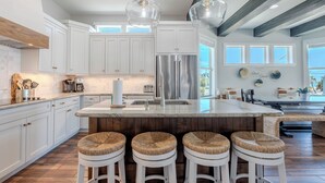 A modern kitchen with white cabinets, a stainless steel refrigerator, and a large island with stools. - Island Grande across the street from beach (Fort Myers Beach)